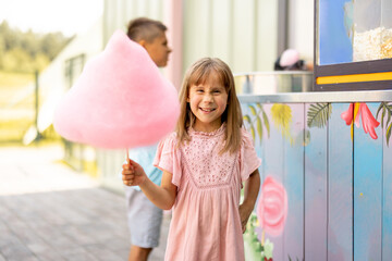 Little happy girl holds pink cotton candy while visiting amusement park during a summer vacation