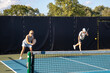 © pics721 - A male pickleball player serves as his female partner stands at the baseline waiting for a return.