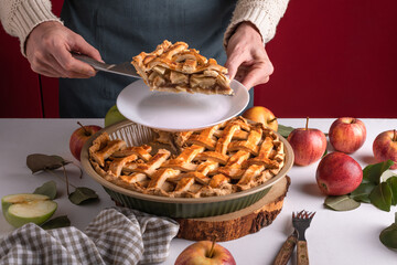 Woman serving a slice of apple pie on a plate, ready to eat. Thanksgiving traditional dessert with red and green apples, Thanksgiving tart preparation, autumn bakery. Crispy weather sweets, recipe