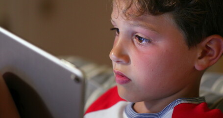 Wall Mural - Young boy playing game online with tablet tech. Child addiction to video-game in competition. Tech native generation