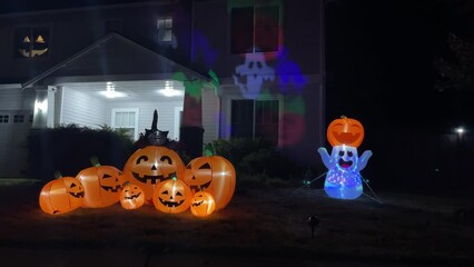 Wall Mural - Illuminated night Halloween house outdoor decorations with inflatable figures of pumpkins, cat and ghost near house