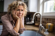© AI_images - A forlorn woman at her kitchen sink looking worried about a plumbing problem.