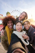 © CarlosBarquero - Vertical excited smiling group multiracial friends taking funny selfie looking at camera standing together outdoor. Multi-ethnic young people in amusement park having fun in sunny winter holiday.