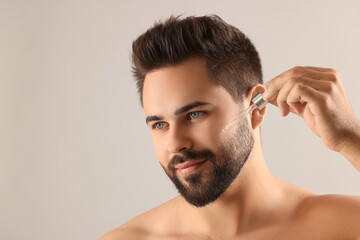 Poster - Handsome man applying cosmetic serum onto face on light grey background, space for text