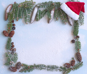 new year winter christmas background. frame of a twig with pine cones on a light blue background in the snow and a Santa hat.