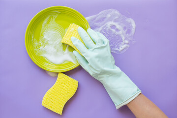 a gloved hand washes a plate. posky top view on a lilac background.