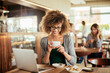 © Geber86 - Young African American woman drinking coffee and using a laptop in a cafe