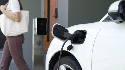 Wall Mural - A woman unplugs the electric vehicle's charger at his residence. Concept of the use of electric vehicles in a progressive lifestyle contributes to a clean and healthy environment.