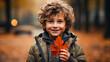 Cute handsome little boy holds an orange maple leaf in his hands. Autumn time, walking outdoors