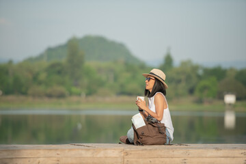 Wall Mural - asian woman traveler with backpack and cup of coffee sitting on quayside relax during coffee break on background summer vacations and lifestyle hiking concept.