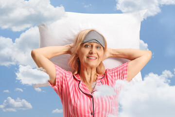 Wall Mural - Mature woman in pajamas with a sleeping mask resting over a pillow among clouds