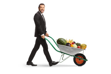 Wall Mural - Full length profile shot of a businessman pushing a wheelbarrow full of fruits and vegetables