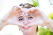 In this captivating close-up, a young woman holds her hands up in a heart shape, framing her face as she looks through the heart with a tender gaze. This image beautifully captures the essence of love