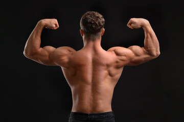 Wall Mural - Muscular man showing his strength on black background, back view. Sexy body