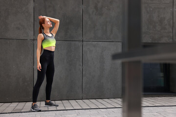 Poster - Beautiful woman in stylish gym clothes posing near grey wall on street