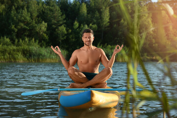 Wall Mural - Man meditating on color SUP board on river