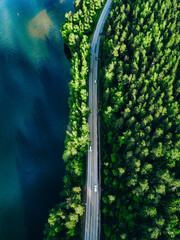 Wall Mural - Aerial view of road with cars between green forest and blue lake in Finland