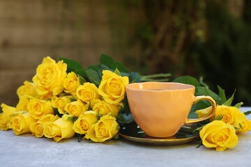 Canvas Print - Cup of drink and beautiful yellow roses on light table outdoors, space for text