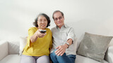 Fototapeta Panele - Happiness asian senior couple sitting on sofa watching TV with relax and enjoy in living room at home, happy family with elderly man and woman watching television, entertainment in weekend.