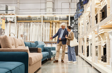 side view full length portrait of senior couple looking at furniture in home improvement store, copy