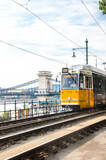 Fototapeta Lawenda - Budapest, Hungary, August 15, 2023. Yellow Tramway and City Chain Bridge in Budapest.