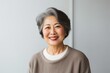 © Anne-Marie Albrecht - Portrait of a Japanese woman in her 50s wearing a chic cardigan against a minimalist or empty room background