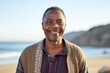 medium shot portrait of a Kenyan man in his 50s wearing a chic cardigan against a beach background