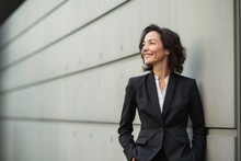 portrait of a Mexican woman in her 50s wearing a sleek suit against a modern architectural background