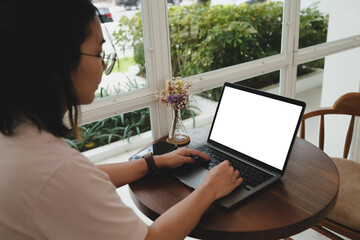 Wall Mural - Close-up of a woman using a laptop, sending messages in the garden while sunbathing. The laptop has a blank screen, and she is texting and making video calls.