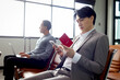 © Stella - Passengers wait for flight, Asian businessman sits at departure terminal airport, holds mobile phone and passport for checking information, travel on holiday vacation or business trip transportation.