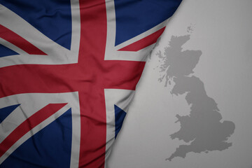 Wall Mural - big waving national colorful flag and map of great britain on the gray background.