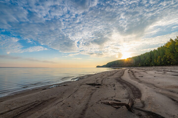 Wall Mural - Sunrise on the river bank sun through the trees, beautiful clouds panoramic view.