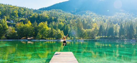 Wall Mural - Happy woman jumping on pier, breathtaking landscape with emerald lake in mountain- Slovenia- freedom,travel,tourism,healthy lifestyle concept