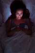 © olga_demina - A woman, shrouded in darkness, stares at her phone while in bed, glimpse into the realms of insomnia and social media obsession.