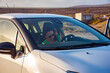 © Mireia - White woman in sunglasses getting into the white car preparing her seat to start driving in a dry brown mountains landscape at sunset.