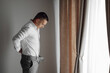 © Vasil - Relaxed man puts on a white shirt and gray pants in a hotel room with natural light. The groom puts on a shirt and prepares for the wedding. Free space