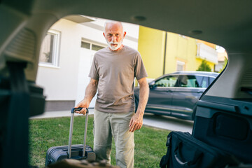 Wall Mural - One senior man travel concept male put suitcase in trunk of the car