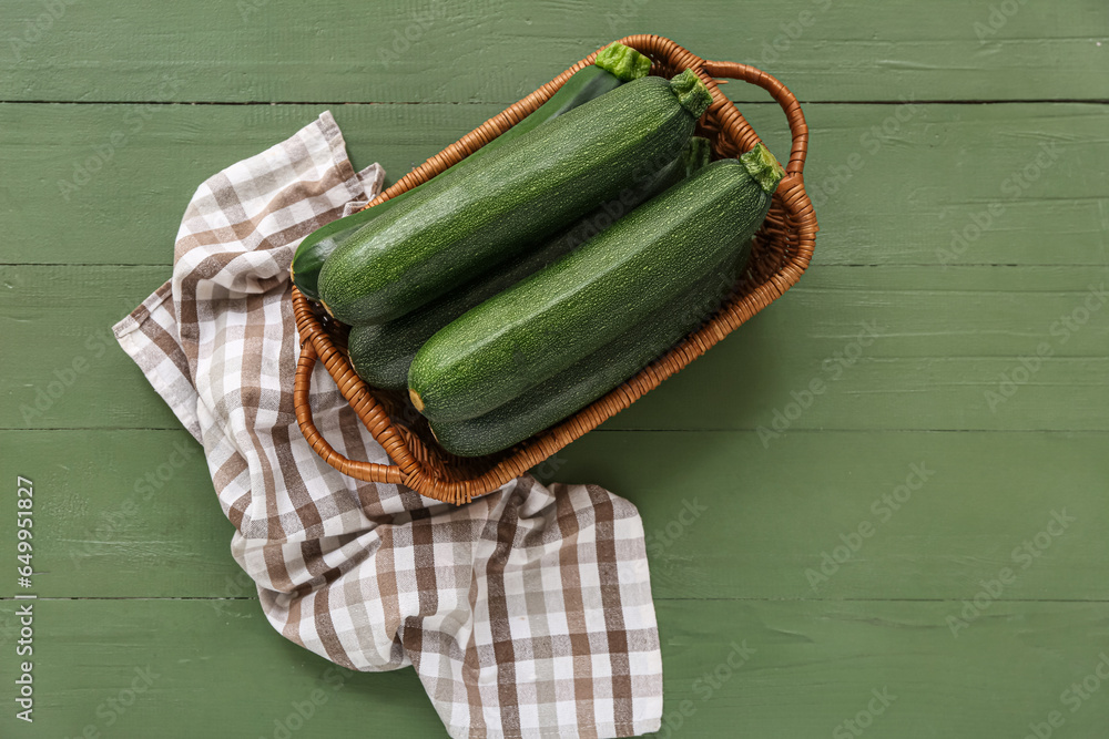 Wicker basket with fresh zucchini on green wooden background