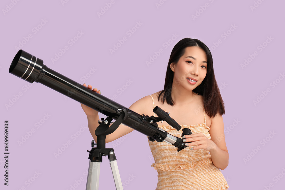 Young Asian woman with telescope on lilac background