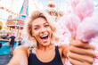 Portrait of beautiful young woman with curly blond hair smiling while holding a pink sweet cotton candy
