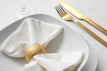 Elegant table setting with golden cutlery and folded napkin on white background, closeup