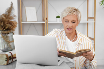 Canvas Print - Mature woman with book learning English language online at home