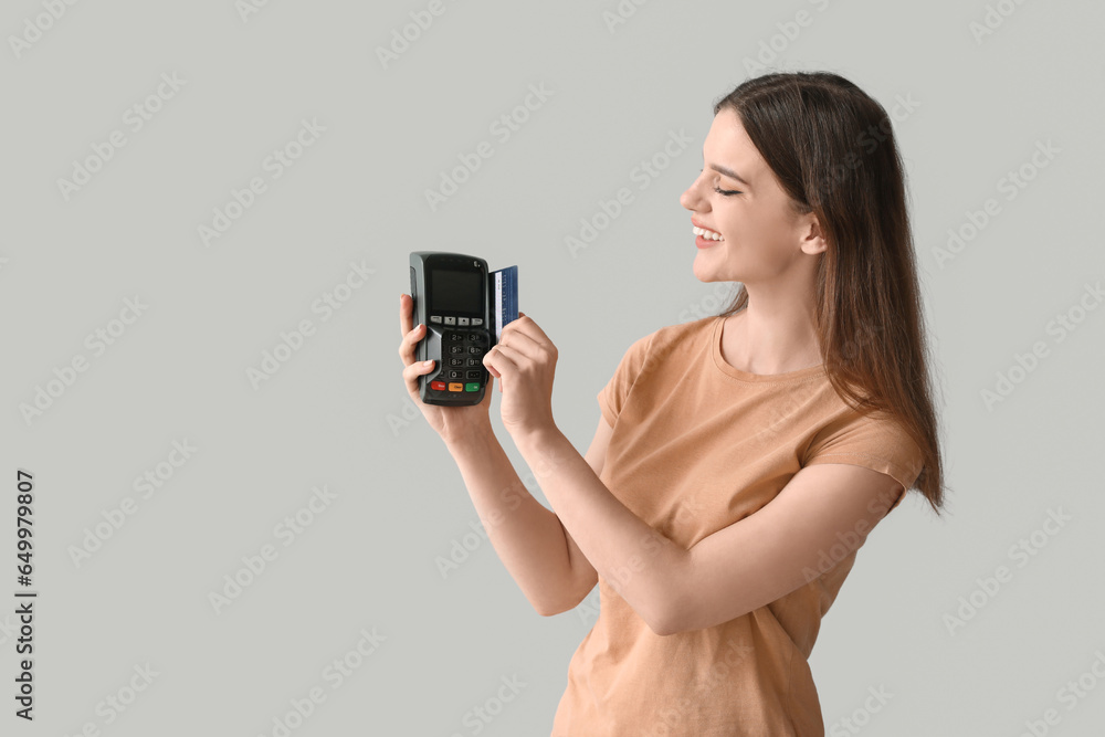 Young woman paying with credit card via terminal on light background
