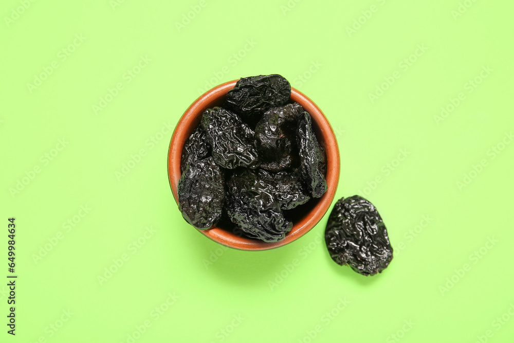 Bowl with tasty dried plums on green background