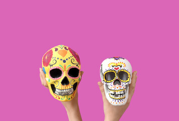 Sticker - Female hands holding painted human skulls for Mexico's Day of the Dead (El Dia de Muertos) on pink background