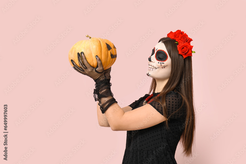 Young woman dressed for Halloween with pumpkin on light background