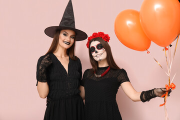 Wall Mural - Young women dressed for Halloween with balloons on light background