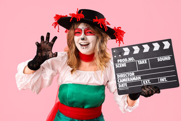 Canvas Print - Young woman with painted skull on her face and clapperboard against pink background. Halloween celebration