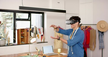 Wall Mural - biracial male fashion designer using virtual reality headset in studio, slow motion