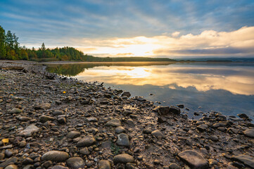 Wall Mural - Golden dawn on the sandy, pebbly riverbank, clouds in the distance, fog, reflection in the water.